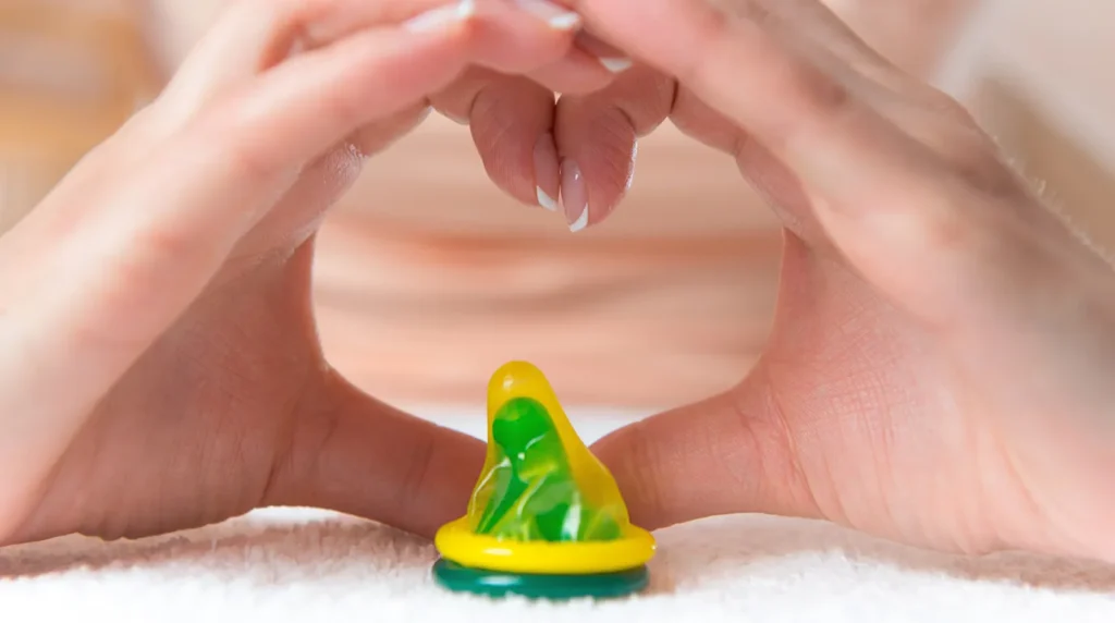 Tangan membentuk simbol hati di atas kondom hijau sebagai simbol sex aman tanpa pengaman