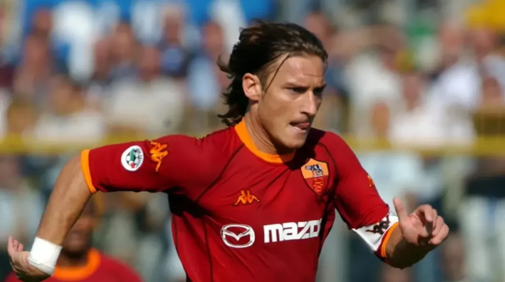 Francesco Totti mengenakan jersi merah AS Roma merayakan gol di lapangan sepak bola.