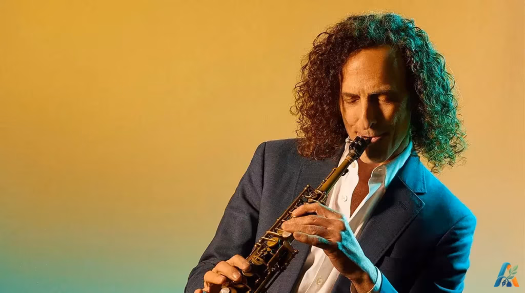 Pemain saksofon Kenny G berambut keriting panjang memegang saksofon dengan latar belakang kuning jingga.
