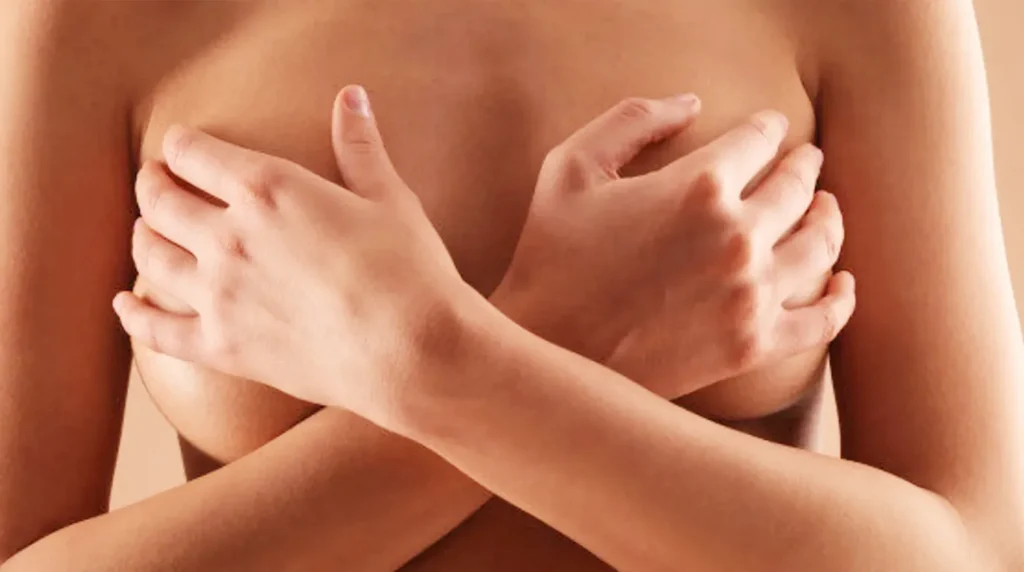Wanita menyilangkan tangan menutupi payudara dengan latar belakang polos.