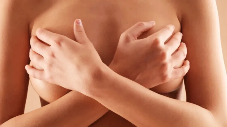 Wanita menyilangkan tangan menutupi payudara dengan latar belakang polos.