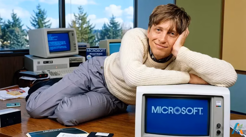 Bill Gates muda berpose bersandar di atas komputer IBM dengan logo Microsoft di layar monitor.
