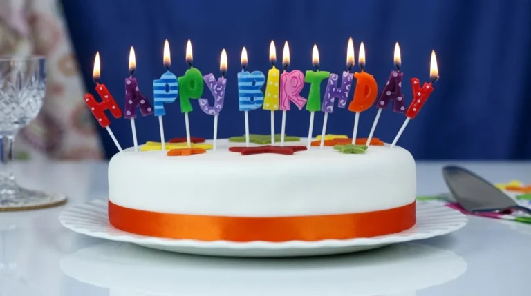 Kue ulang tahun putih dengan lilin berwarna-warni membentuk tulisan Happy Birthday yang menyala terang, menciptakan suasana perayaan yang ceria.