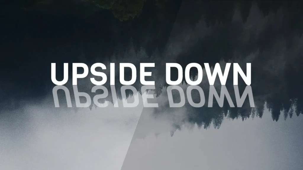 Tipografi teks UPSIDE DOWN dengan efek refleksi terbalik di atas latar belakang siluet hutan pinus kabur, dari file upside-down.webp