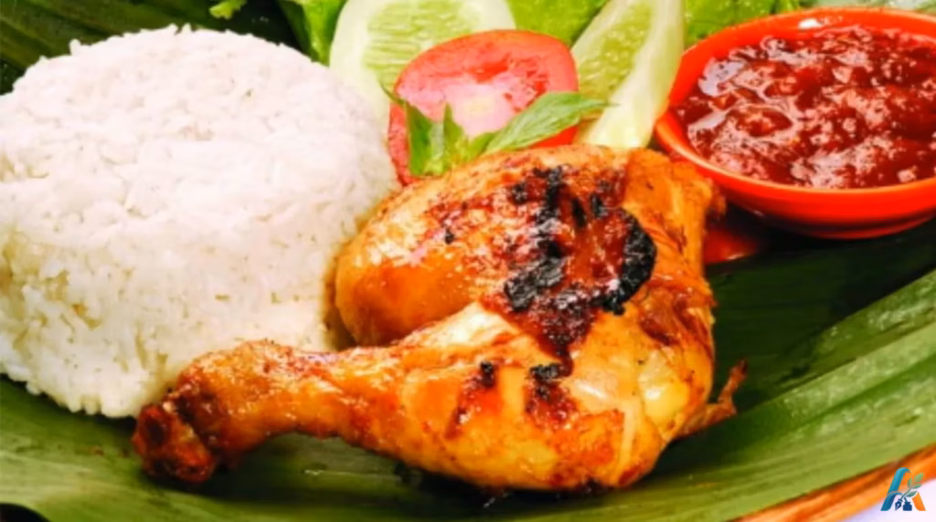 Nasi ayam bakar dengan lalapan tomat, mentimun, daun kemangi, dan sambal merah disajikan di atas daun pisang.