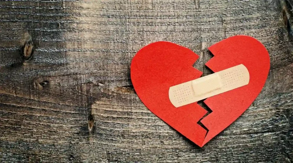 Hati kertas merah yang terbelah dan ditempel plester di atas permukaan kayu, simbol penyembuhan untuk cara-mengobati-patah-hati-dalam-7-hari.webp.