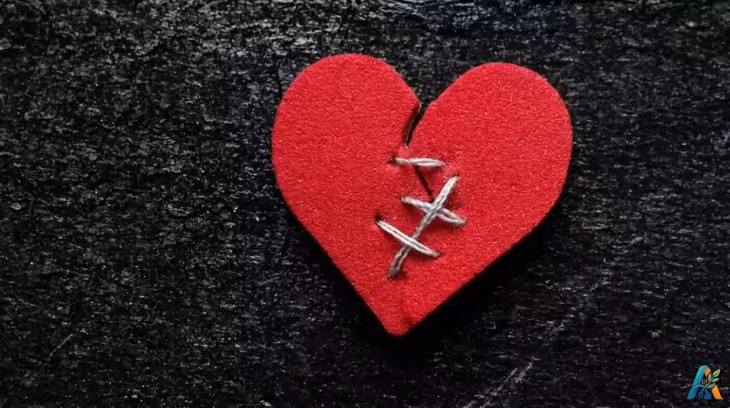 Konsep fixing a broken heart dengan simbol hati merah yang retak dan dijahit menggunakan benang putih