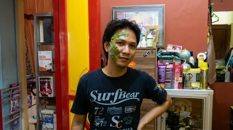 Seorang pria dengan daun hijau di wajahnya sebagai pengobatan tradisional untuk sakit gigi, di dalam sebuah rumah.