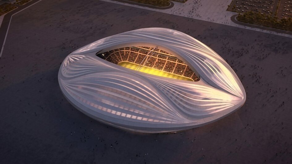 Stadion Al Janoub Qatar tampak atas dengan arsitektur futuristik putih berbentuk dhow saat senja dan lampu lapangan menyala.