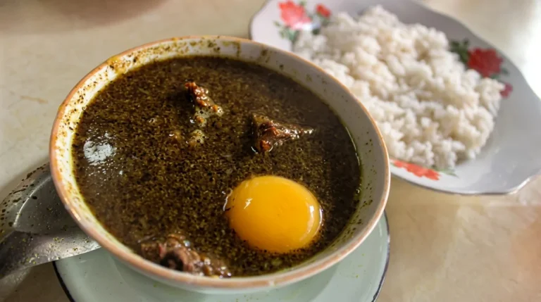 Semangkuk Pallu Basa khas Makassar dengan kuah rempah pekat dan kuning telur mentah, disajikan bersama sepiring nasi putih hangat.