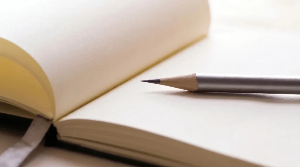 Sebuah pensil tergeletak di atas buku catatan terbuka dengan halaman kosong, melambangkan awal dari sebuah tulisan atau karya sastra yang belum selesai.