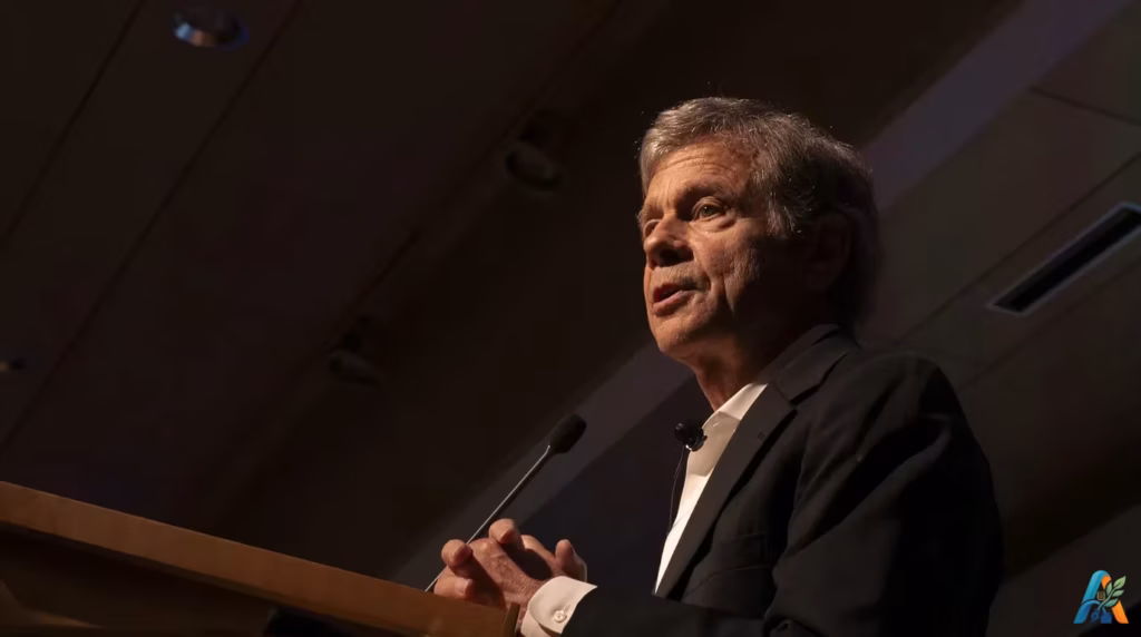 Alan Lightman memberikan ceramah atau kuliah umum di balik podium dengan jas hitam