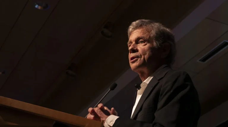 Alan Lightman memberikan ceramah atau kuliah umum di balik podium dengan jas hitam
