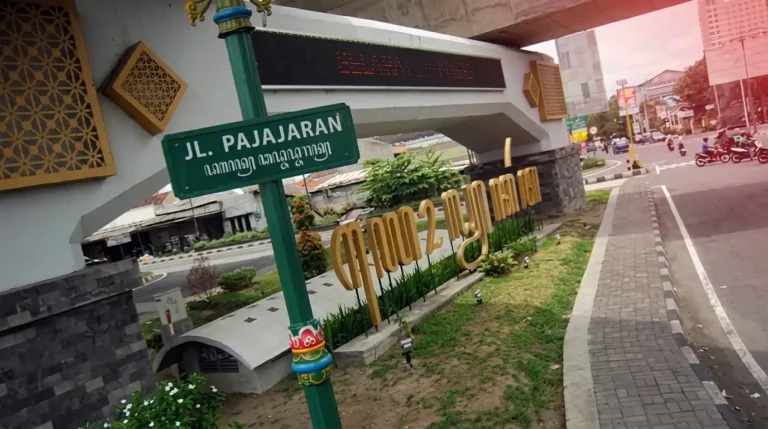 Plang nama jalan Jl. Pajajaran dengan tulisan aksara Jawa di Yogyakarta, menampilkan suasana kota dengan nuansa budaya lokal yang khas.