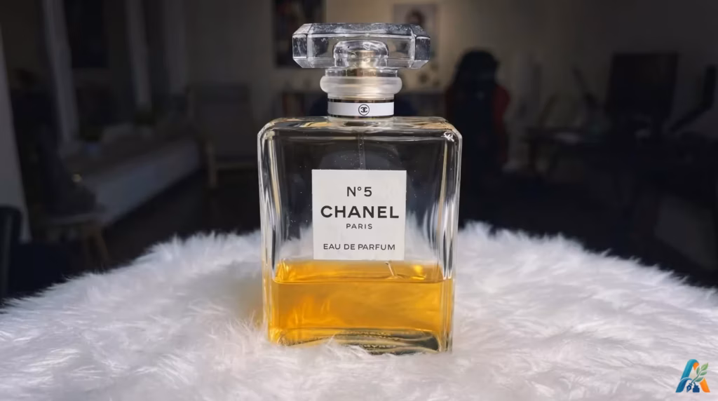 Botol parfum Chanel No. 5 yang elegan dengan cairan keemasan, diletakkan di atas alas bulu putih yang lembut, menampilkan kemewahan klasik.