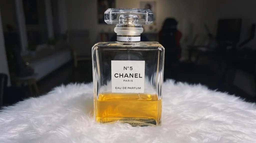 Botol parfum Chanel No. 5 yang elegan dengan cairan keemasan, diletakkan di atas alas bulu putih yang lembut, menampilkan kemewahan klasik.