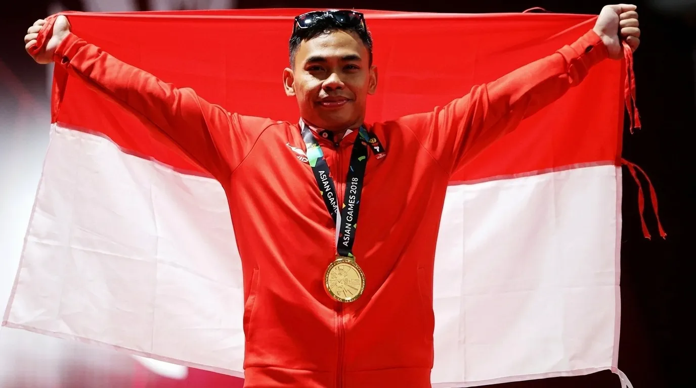 Atlet Indonesia Eko Yuli Irawan merayakan kemenangan dengan bendera merah putih setelah meraih medali emas di Asian Games, simbol kebanggaan bangsa.