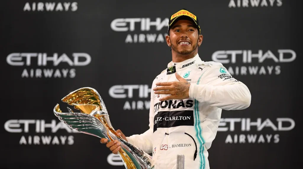 Lewis Hamilton tersenyum memegang trofi juara F1 dengan latar belakang logo Etihad Airways