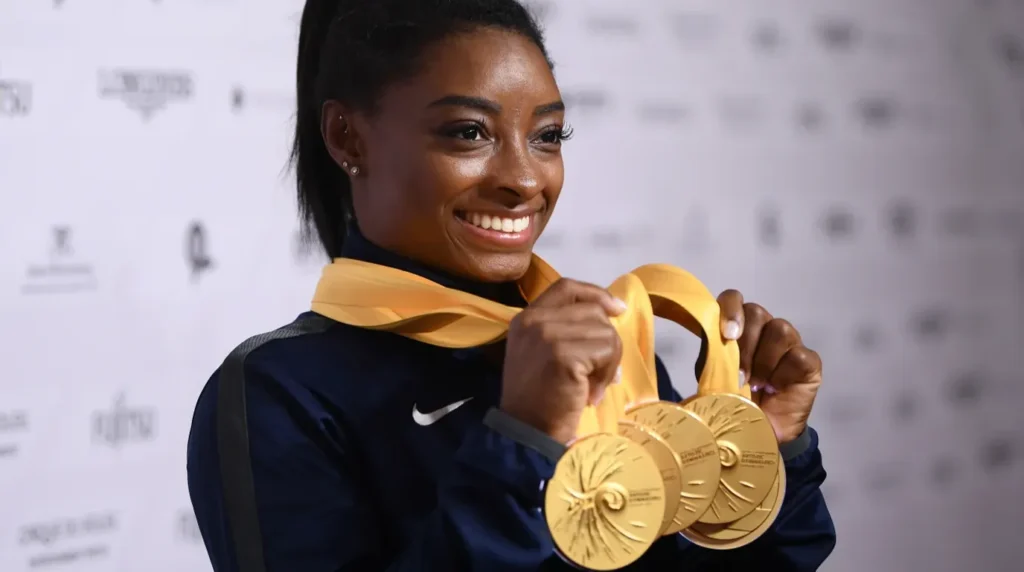 Simone Biles tersenyum gembira memegang empat medali emas bergaya