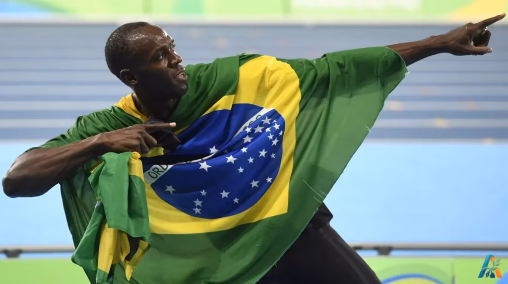 Usain Bolt merayakan kemenangan di lintasan lari dengan menyampirkan bendera Brasil di bahunya dan berpose ikonik menunjuk ke atas.