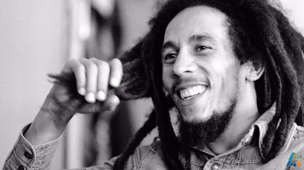 Potret hitam putih ikonik Bob Marley tersenyum sambil memegang rambut gimbalnya, menginspirasi kekuatan dan ketangguhan hidup