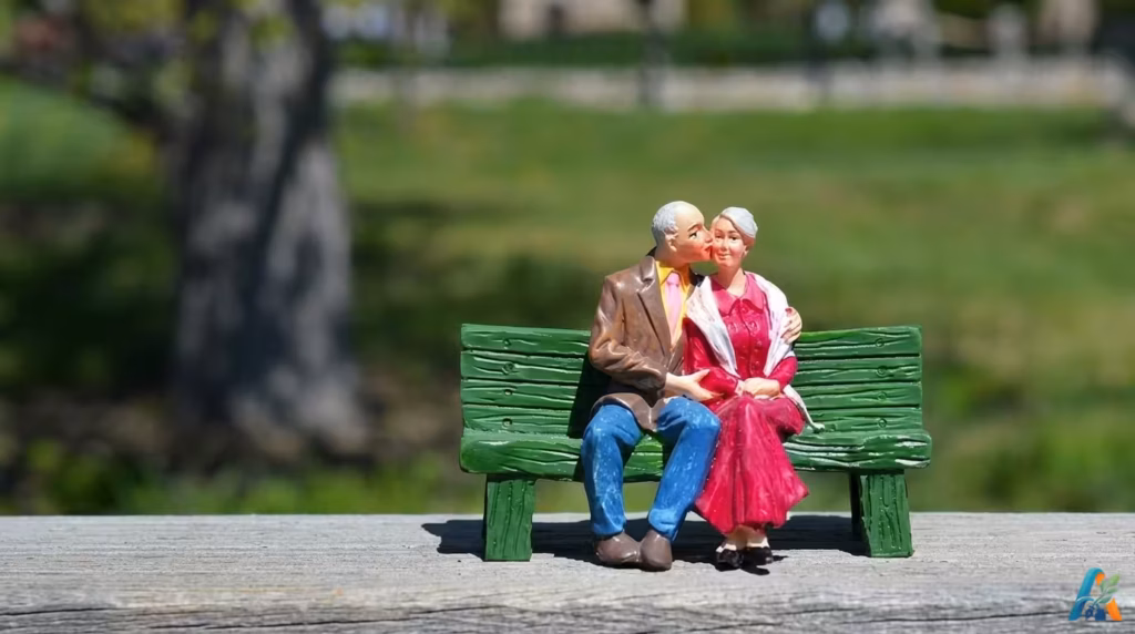 Miniatur sepasang kakek dan nenek duduk di bangku taman hijau, pria mencium pipi wanita, melambangkan kasih sayang di masa tua.