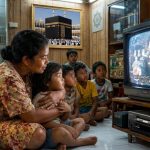Seorang ibu membacakan subtitle film kungfu kepada anak kecil di ruang keluarga sederhana, sementara beberapa anak tetangga duduk di lantai menonton televisi tabung dengan video Betamax di bawahnya, dalam suasana malam yang hangat dan penuh nostalgia.